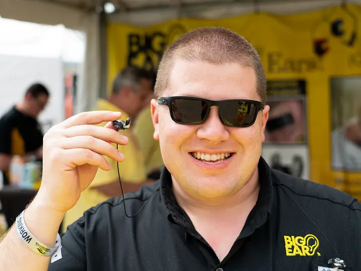 Smiling Big Ear team member in sunglasses holding up a custom earplug at an event booth