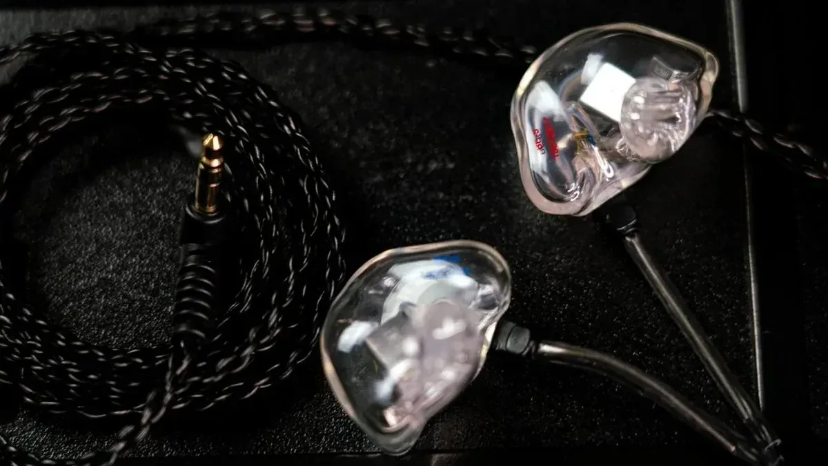 A pair of Big Ear five-driver custom in-ear monitors, drivers visible through the clear shells, braided cable