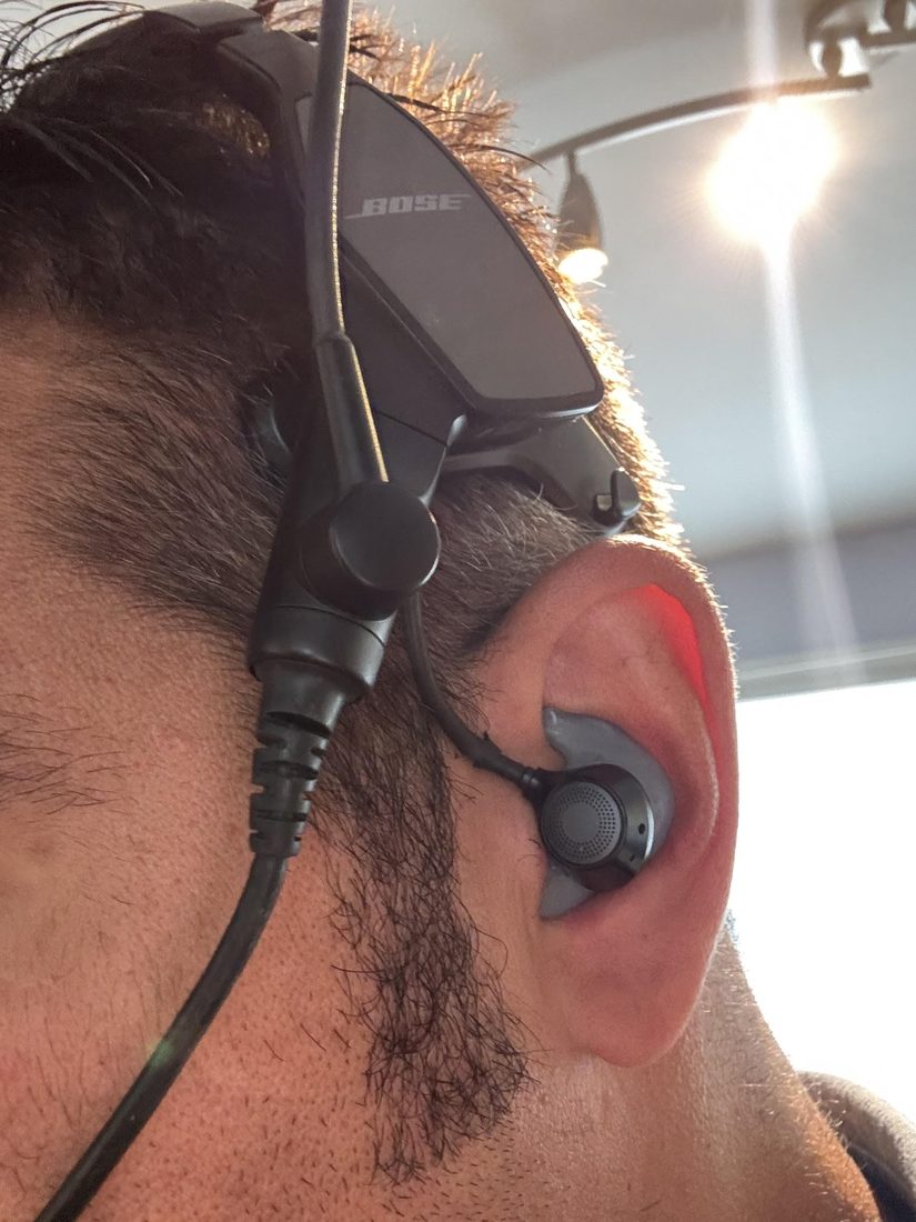 Close-up of a pilot wearing a Bose ProFlight with a custom Big Ear adapter, backlit
