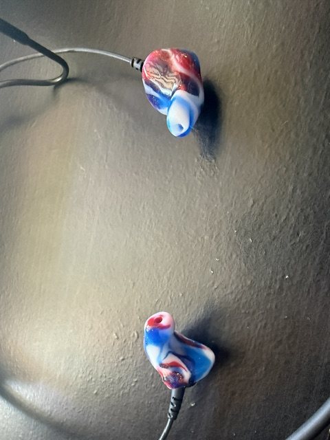 A pair of custom Big Ear Clarity Aloft adapters in a red, white and blue swirl on a tabletop