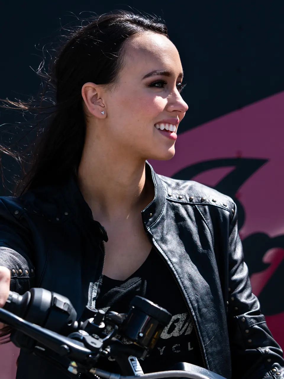 Smiling rider in a leather jacket on her motorcycle with a clear Big Ear custom earplug in her ear