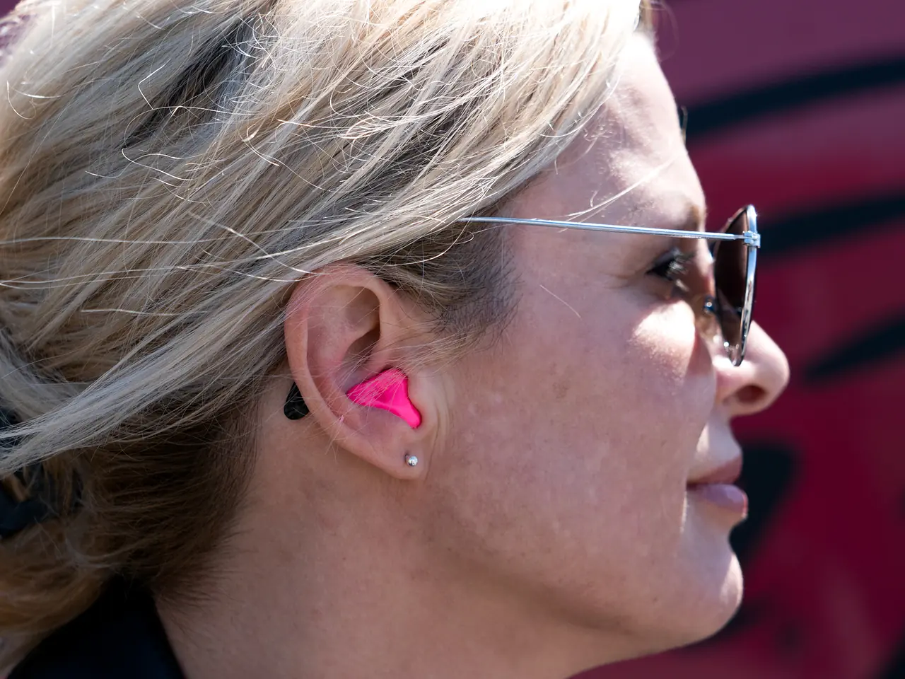 Motorcycle rider in sunglasses wearing a pink Big Ear custom-molded earplug that sits flush inside her ear