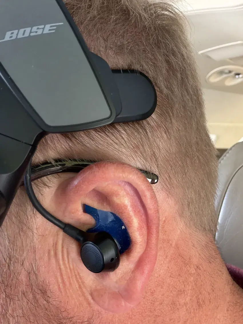 A pilot wearing the Bose ProFlight with a blue custom Big Ear adapter in the cockpit