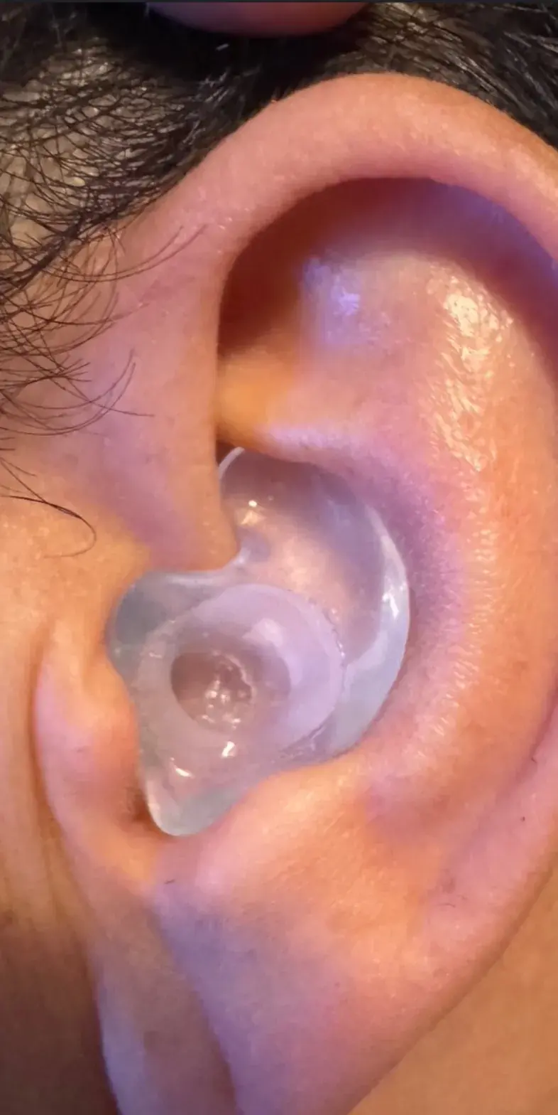 A clear custom Big Ear Bose ProFlight adapter seated in the ear, showing the sound bore