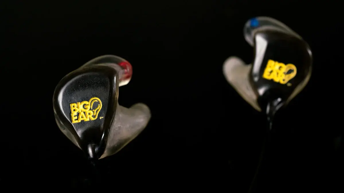 A pair of Big Ear custom in-ear monitors in smoke black with the yellow logo — studio shot on black