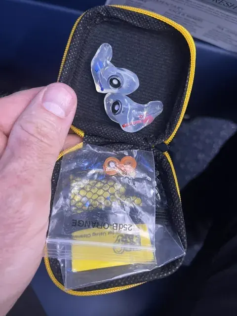 A clear custom The One filtered earplug pair in its case with a 25 dB orange filter set