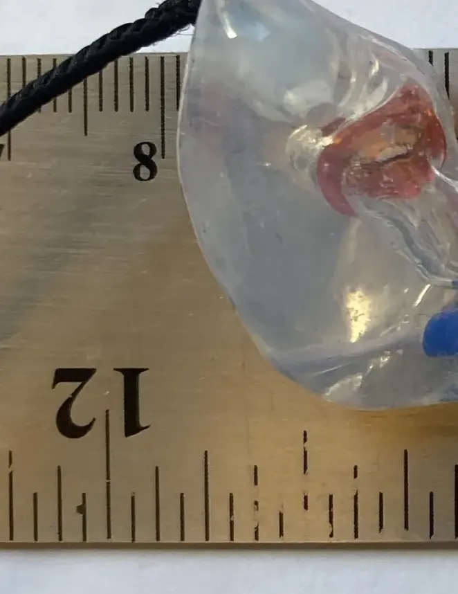 A clear custom The One filtered earplug beside a ruler showing its small size
