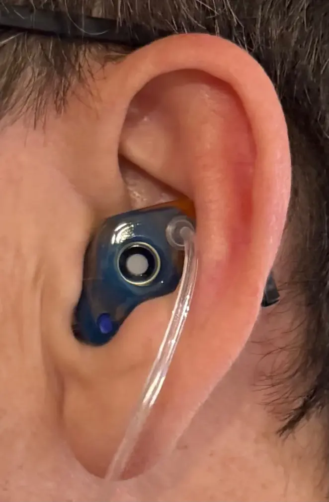 A customer wearing a blue full shell filtered earplug with a clear tube