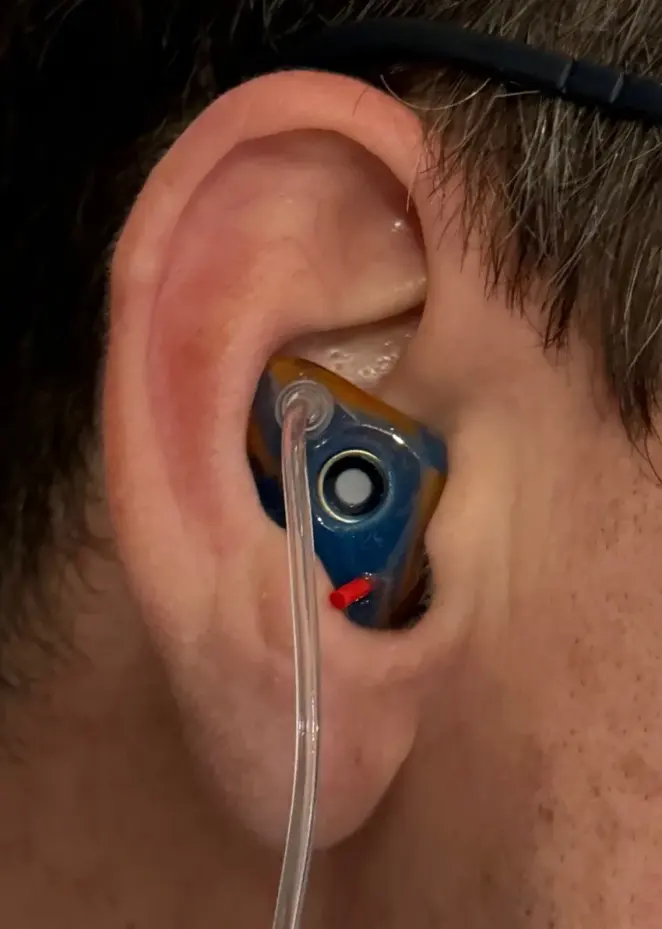 Close-up of a blue and amber custom The One filtered earplug with the filter visible