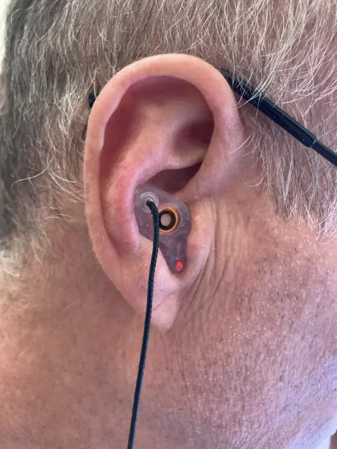 A customer wearing a clear custom The One filtered earplug with the filter and cord