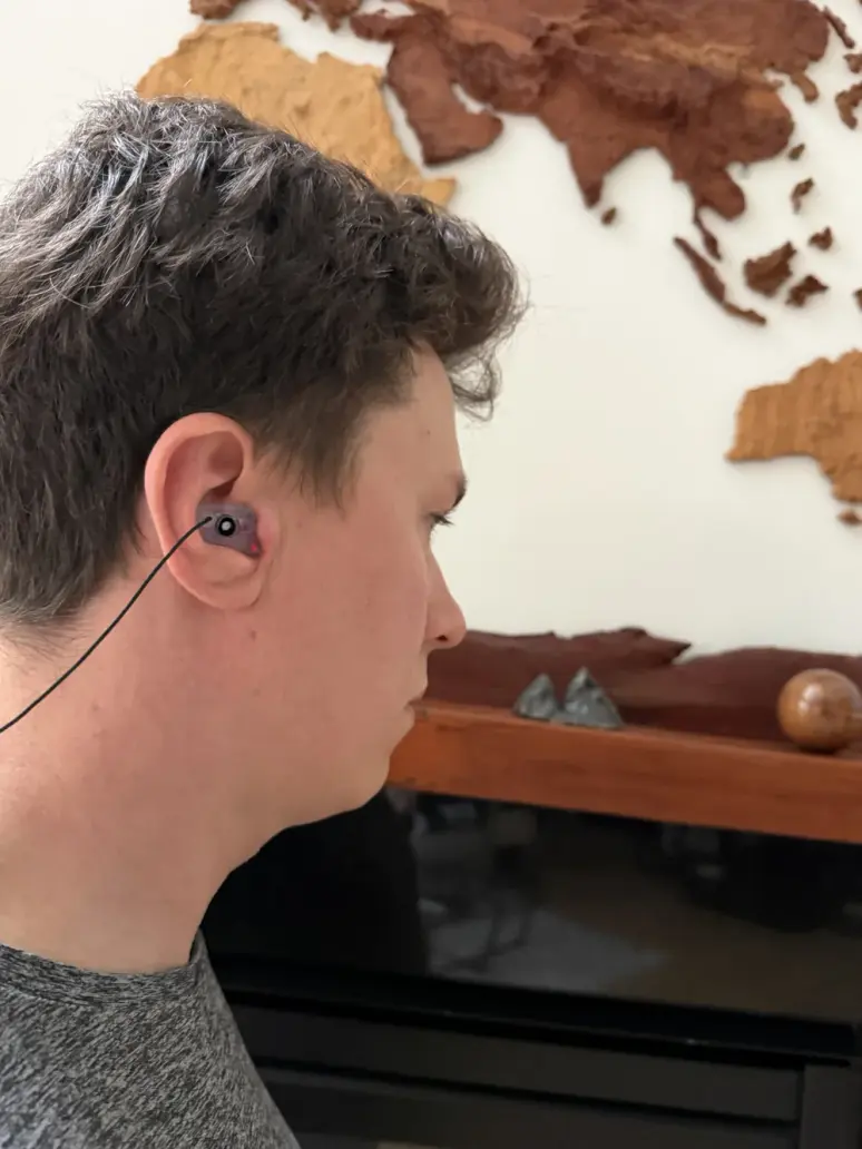 Side view of a customer wearing a dark half shell filtered earplug on a cord